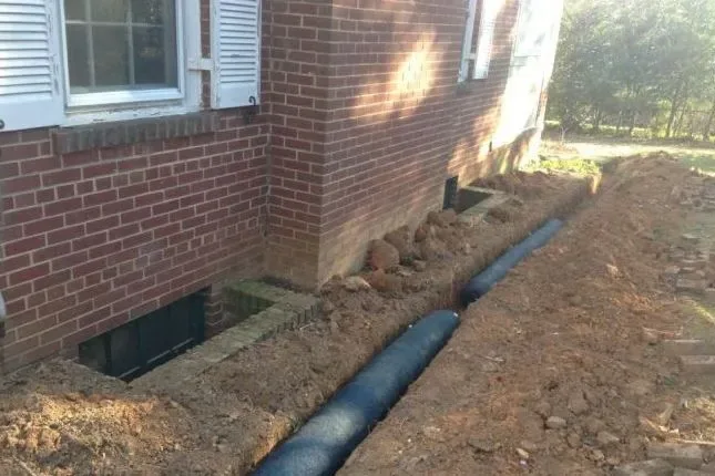 Drainage pipe laid in a trench along a brick house foundation